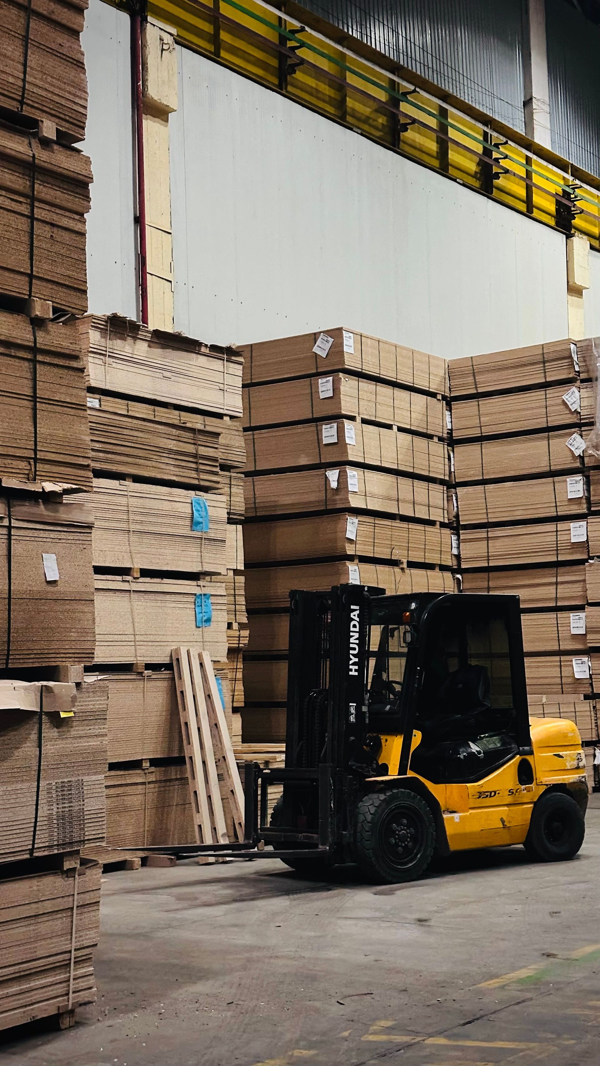 A yellow forklift organizes large stacks of cardboard boxes in a spacious warehouse.